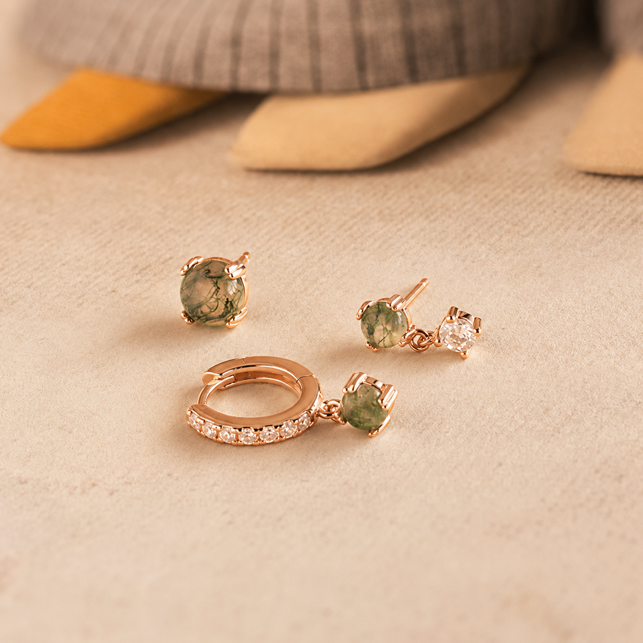 Rose gold earrings with green gemstones on a beige surface